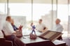 Zwei Superhelden-Spielfiguren sind im Vordergrund zu sehen. Im Hintergrund unterhalten sich die Geschäftsführer.