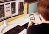 Mann arbeitet mit einem Smartphone und einem Computer am Schreibtisch
